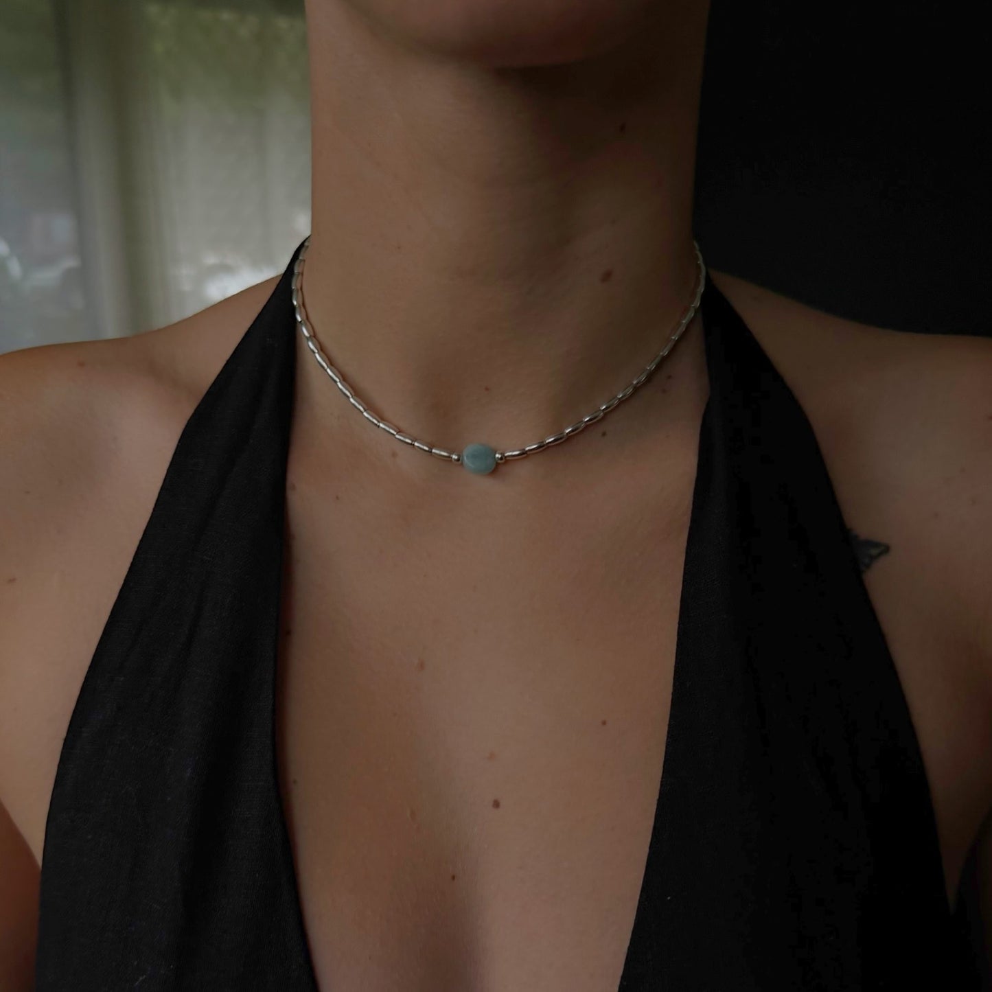 Necklace with a blue pendant worn by a person in a black top.