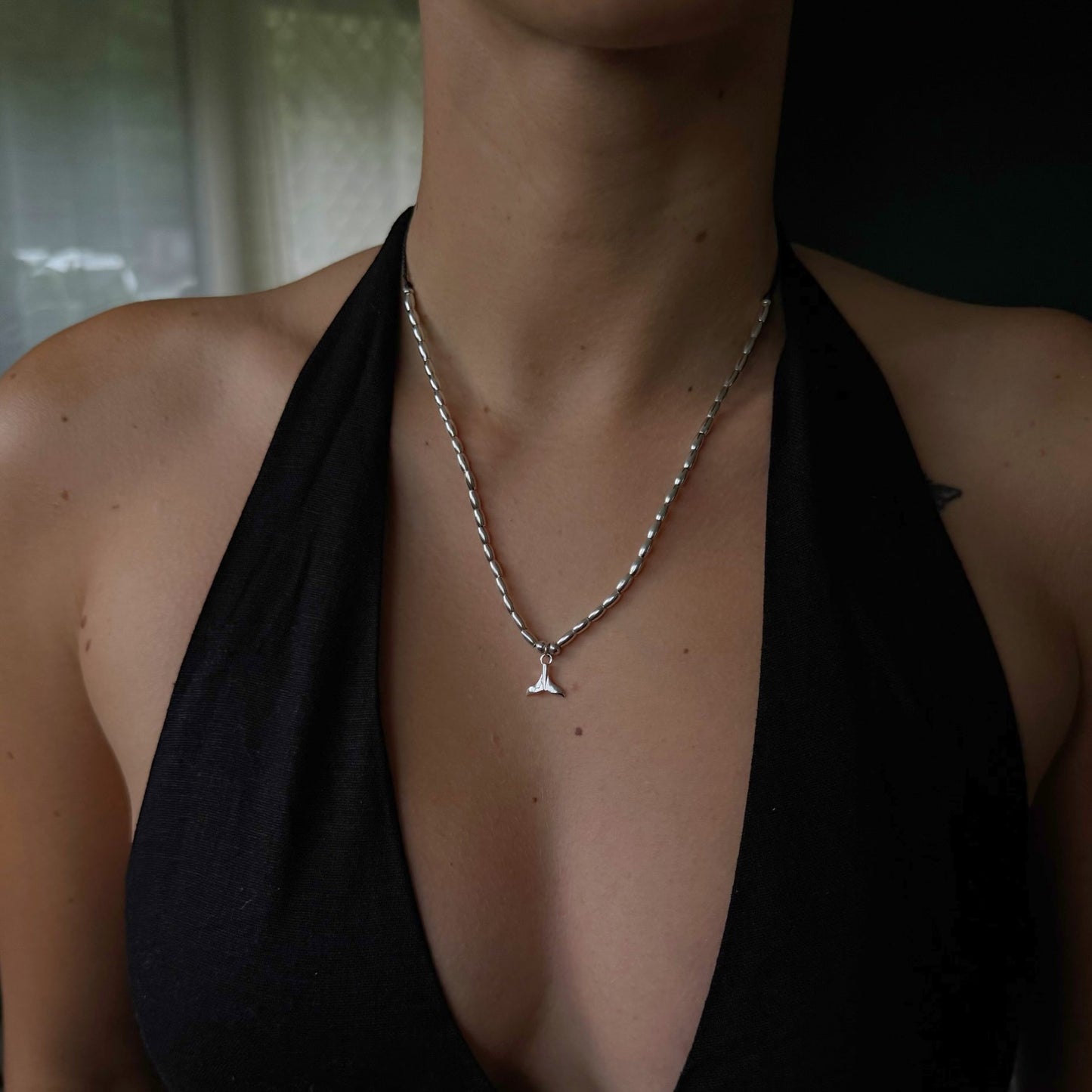 Person wearing a silver necklace with a small pendant