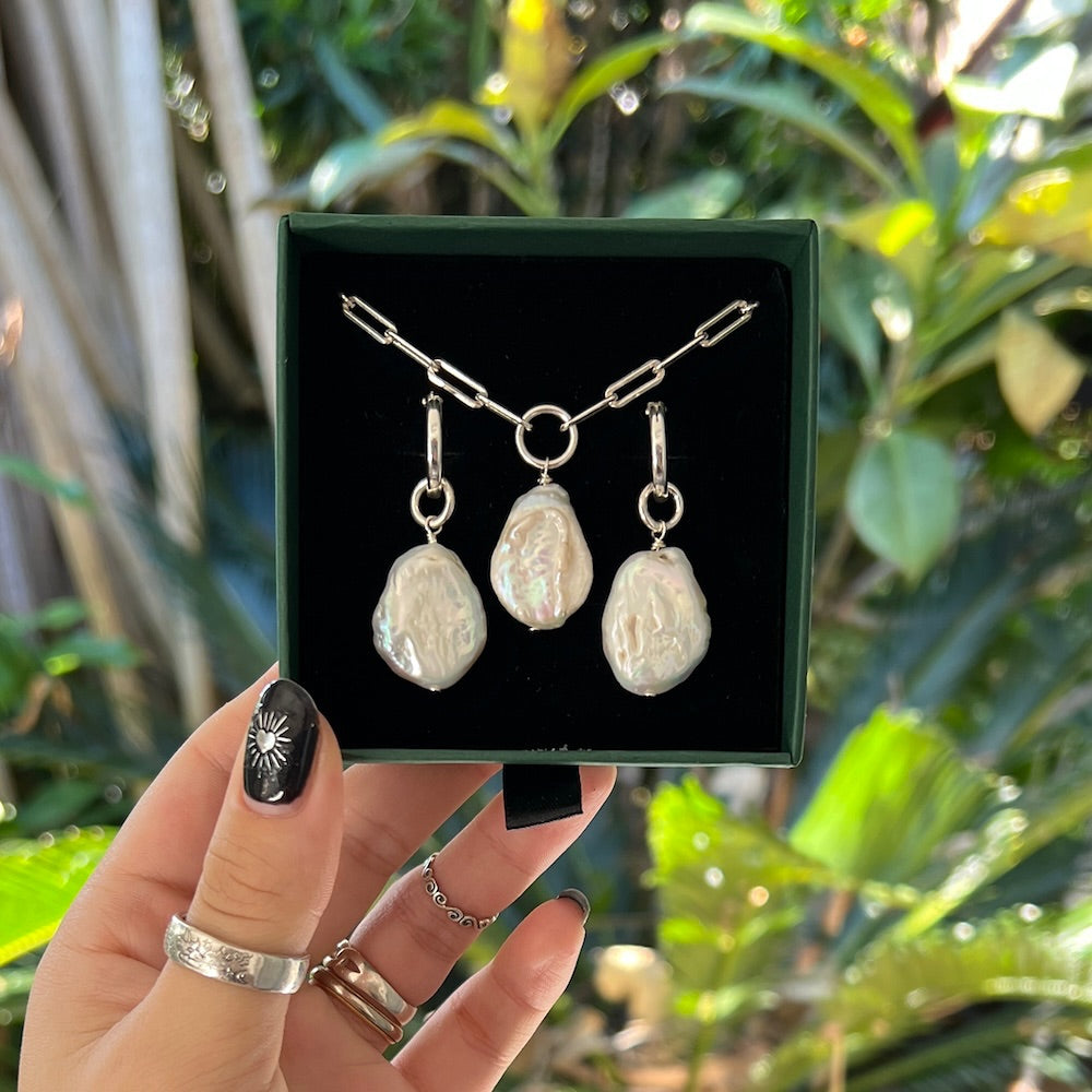 Jewelry set with pearls held in a hand against a green leafy background