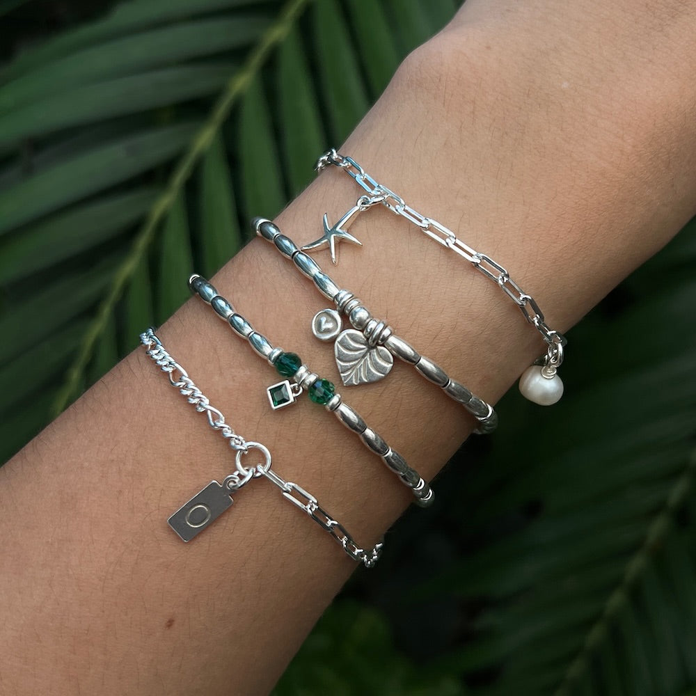 Silver bracelets with various charms on a wrist against a green leafy background