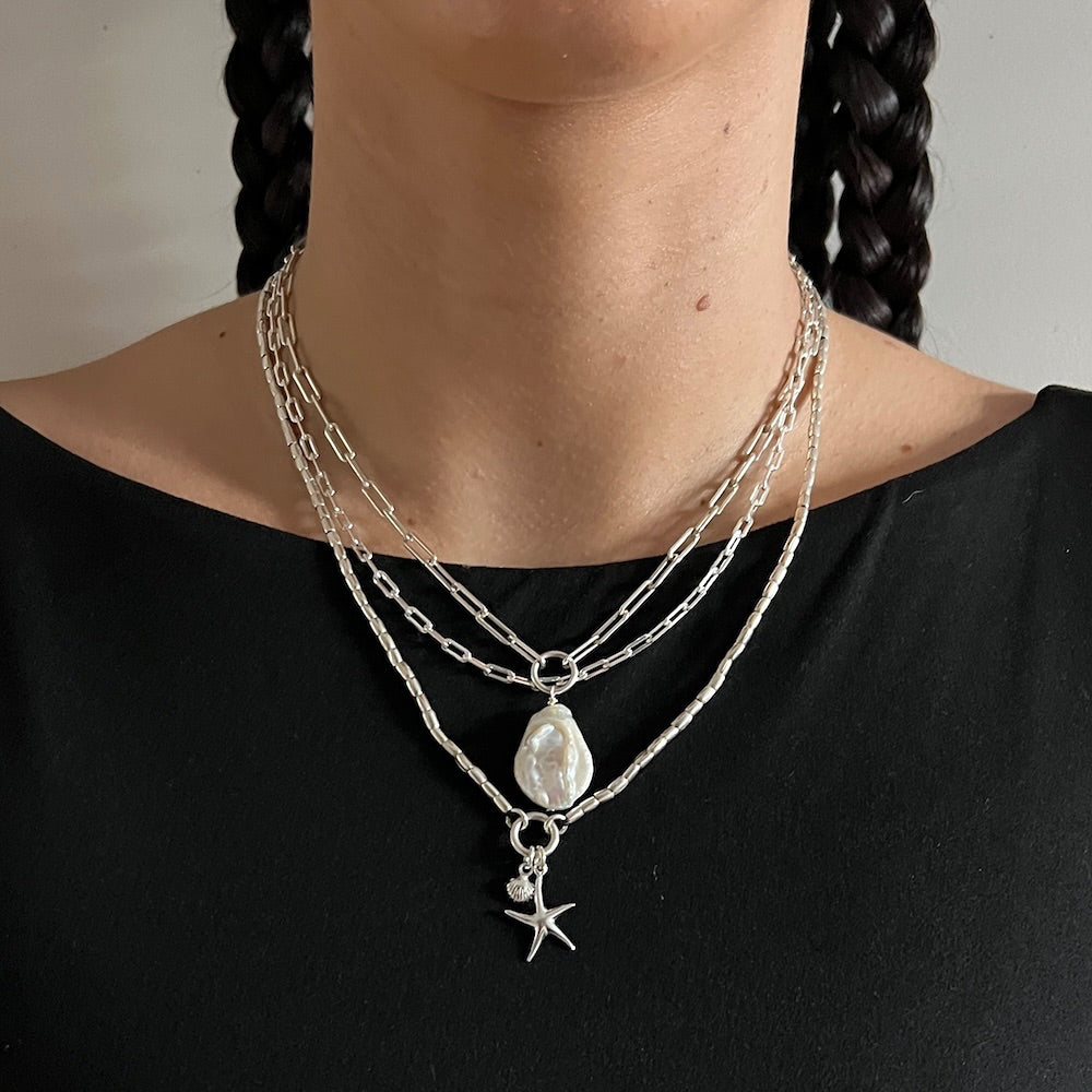 Person wearing a layered silver necklace with a pendant on a plain background