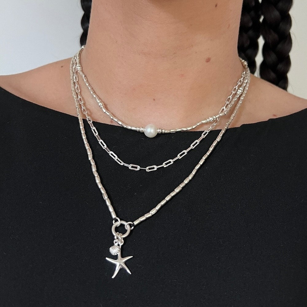 Layered silver necklaces with a starfish charm on a black top against a neutral background