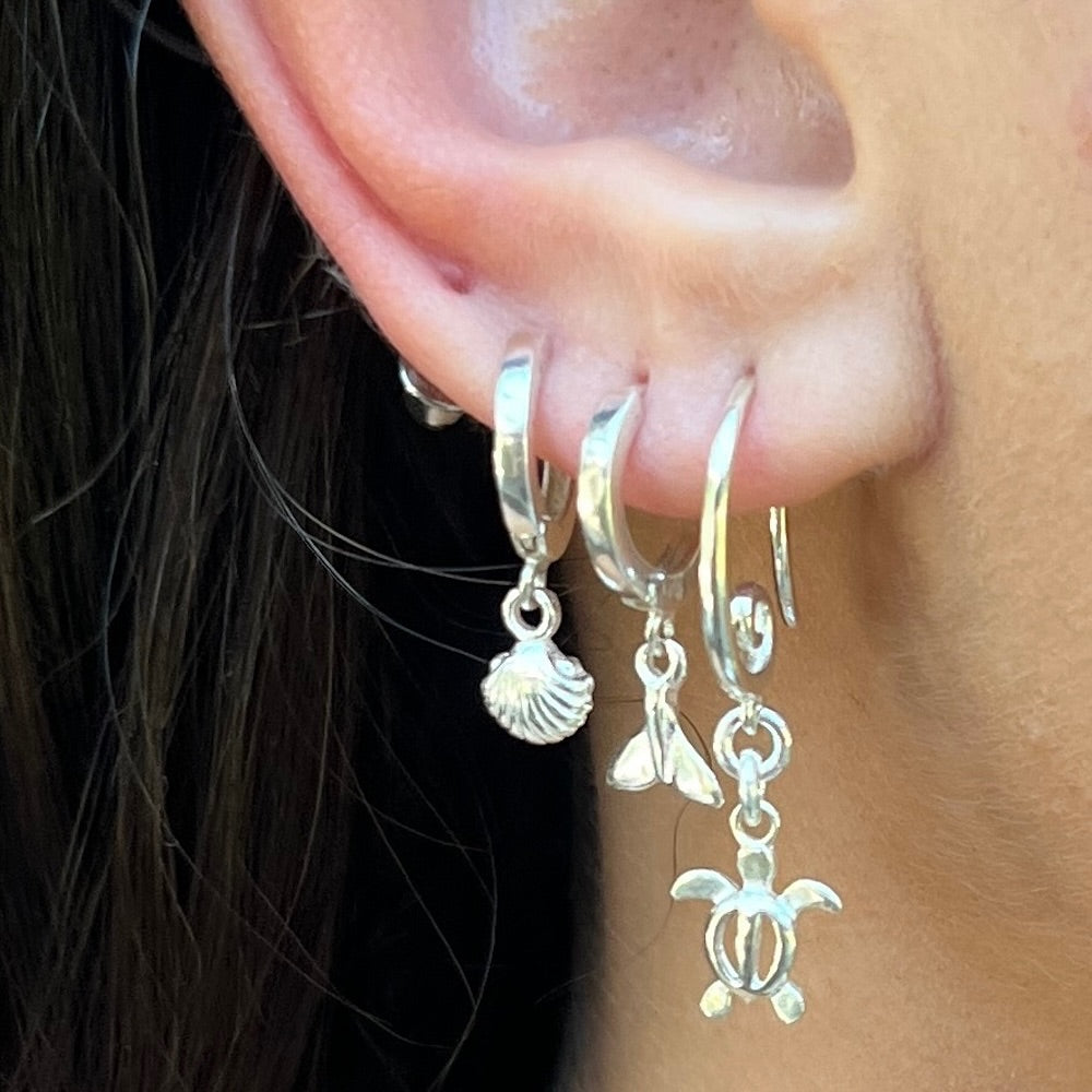 Close-up of an ear wearing silver hoop earrings with charms.