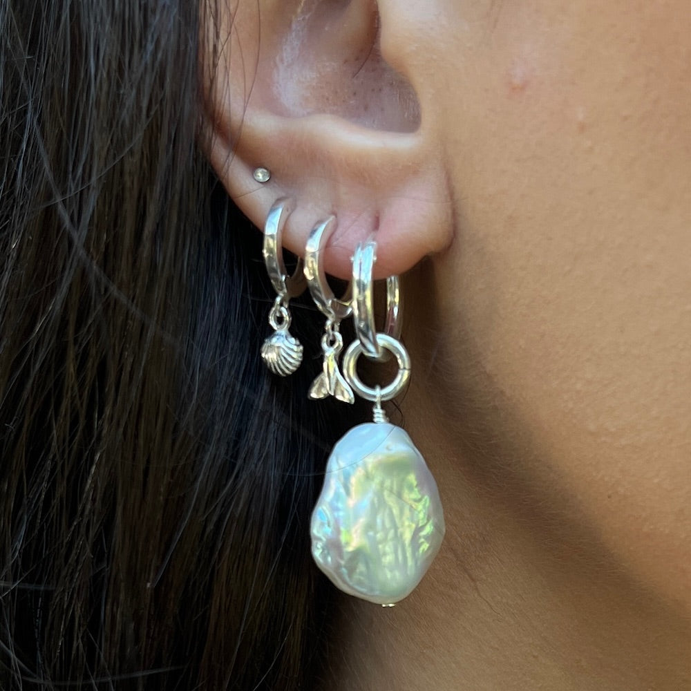 Close-up of an ear wearing multiple silver hoop earrings with charms.