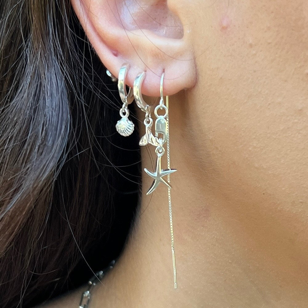 Close-up of an ear wearing silver hoop earrings with starfish charm and chain.
