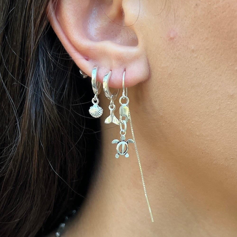 Close-up of an ear wearing silver hoop earrings with charms.