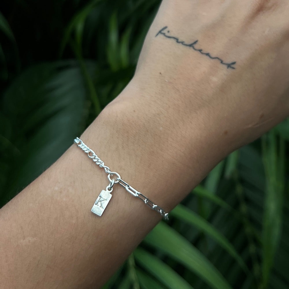 Silver bracelet with a tag on a wrist against a green leafy background