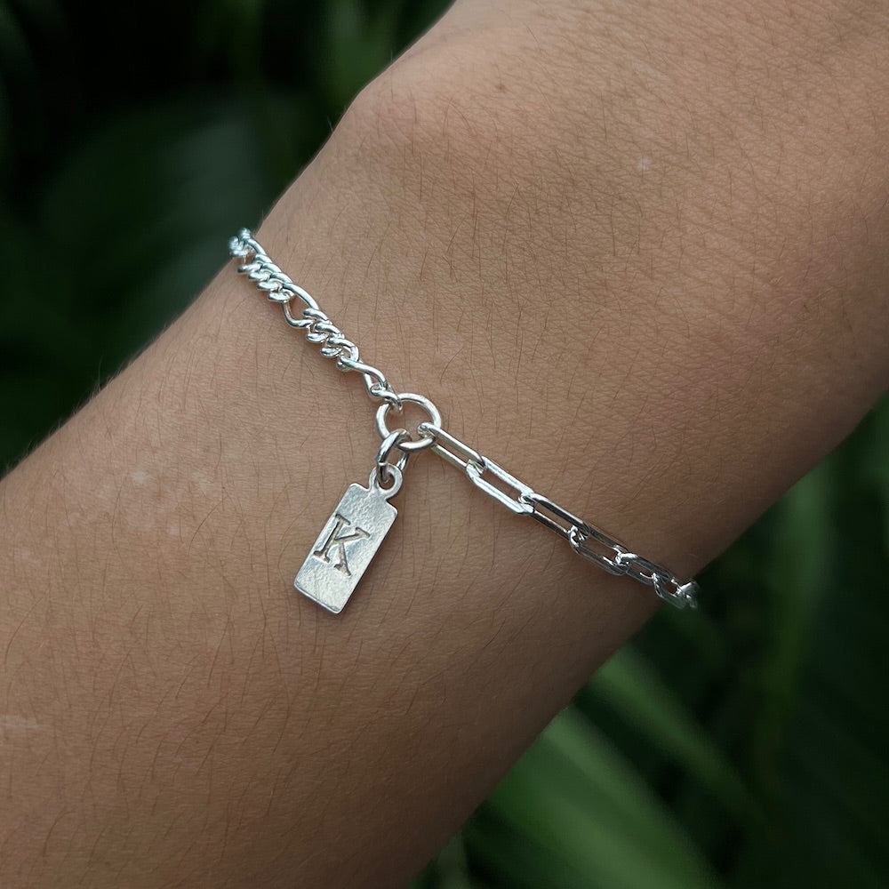 Silver bracelet with a charm on a wrist against a blurred green background
