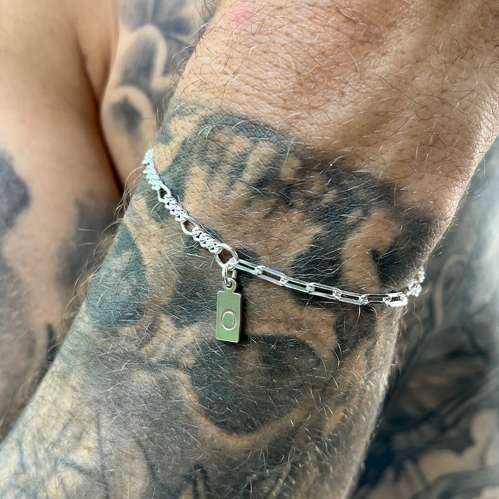 Silver chain bracelet with a green tag on a tattooed arm