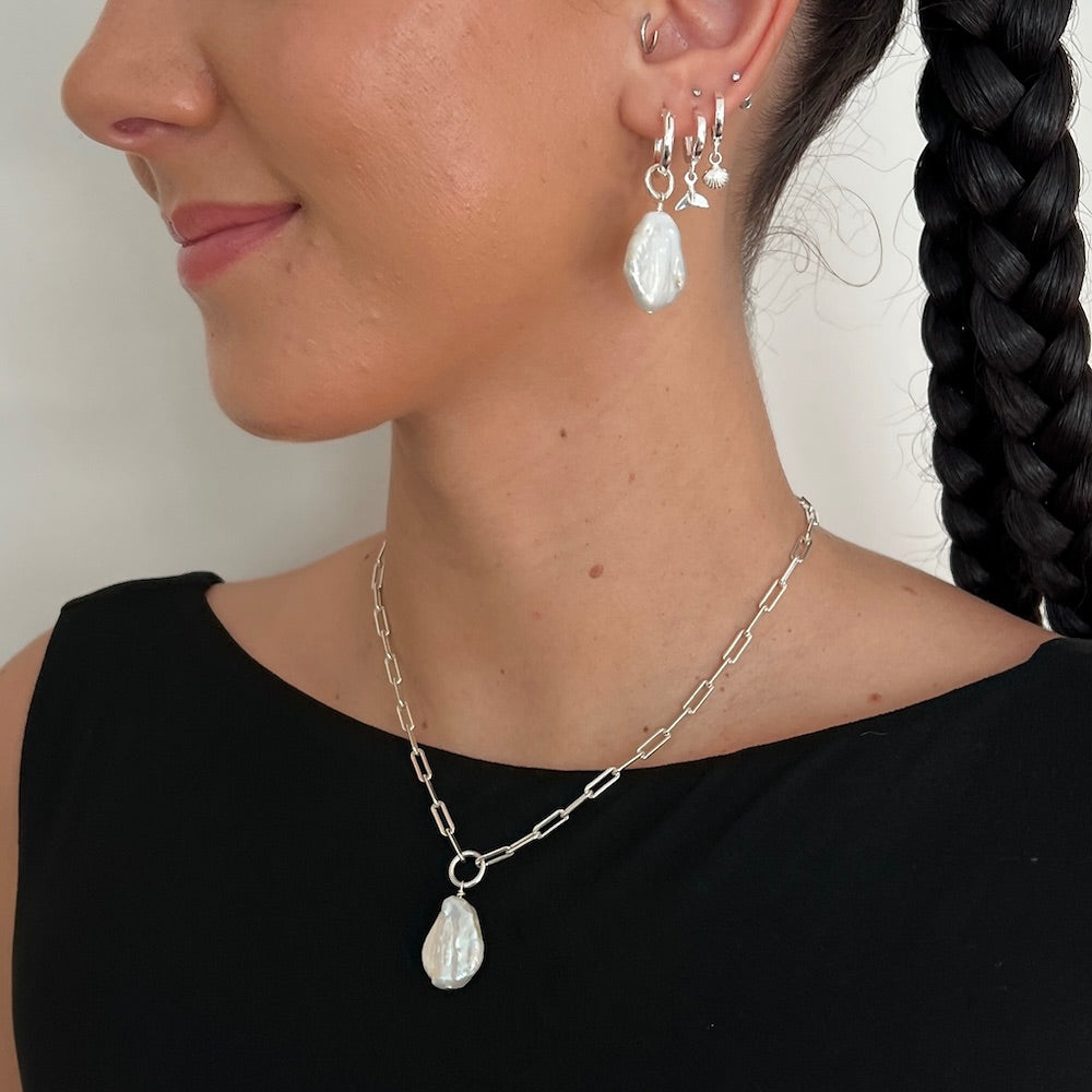 Close-up of a person wearing silver earrings and necklace with a plain background