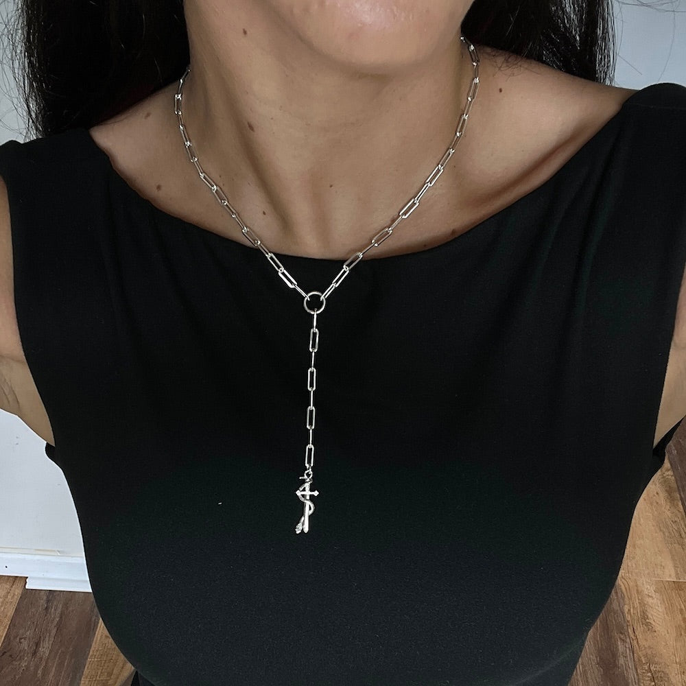 Person wearing a silver chain necklace with a pendant on a plain background
