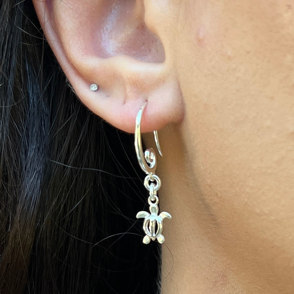 Silver turtle earring worn on an ear with dark hair.