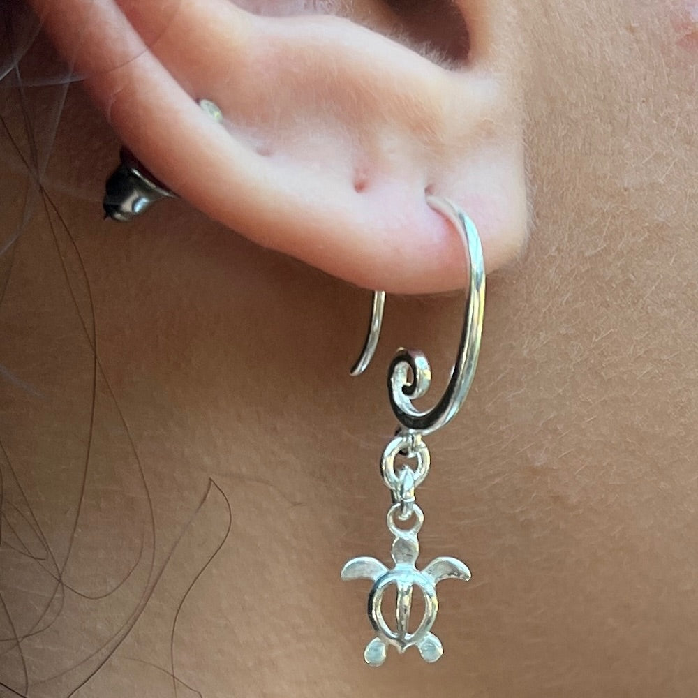Silver turtle charm earring worn on a person's ear.
