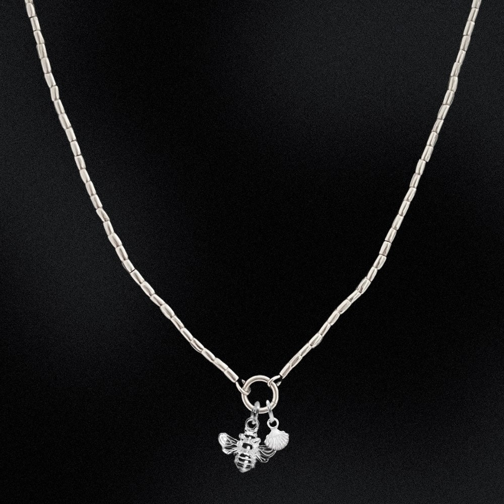 Silver necklace with a bee and fish charm on a black background