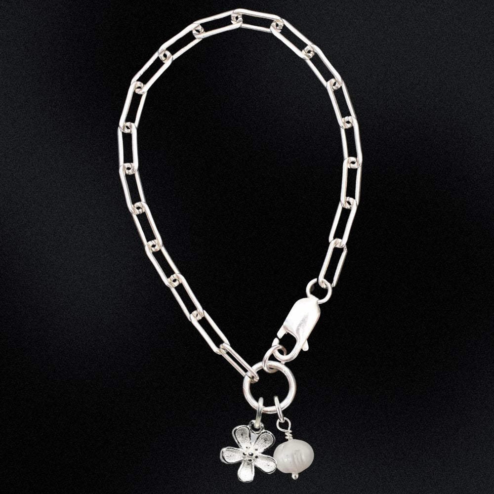 Silver chain bracelet with a flower charm on a black background