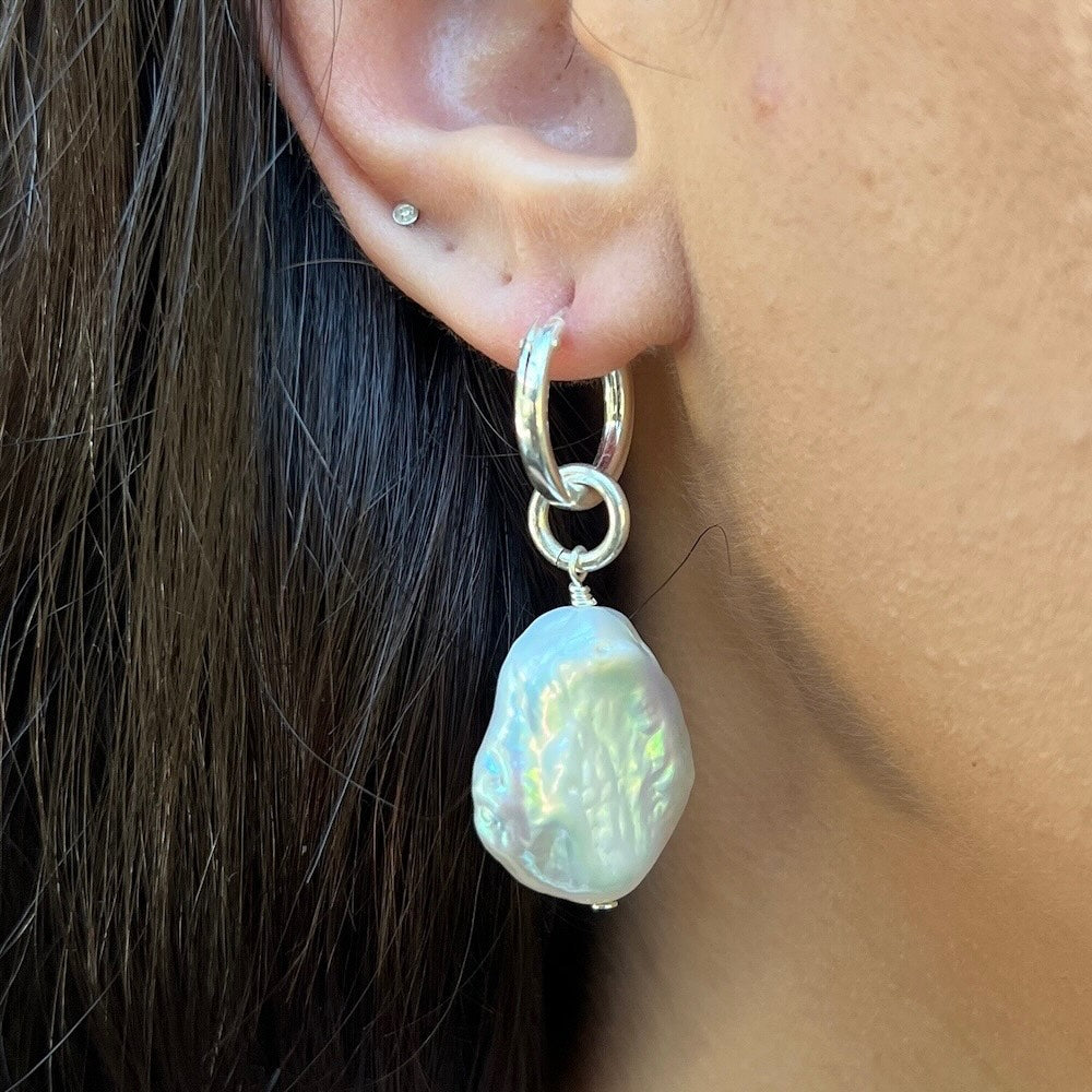 Silver hoop earring with a large pearl pendant worn by a person.