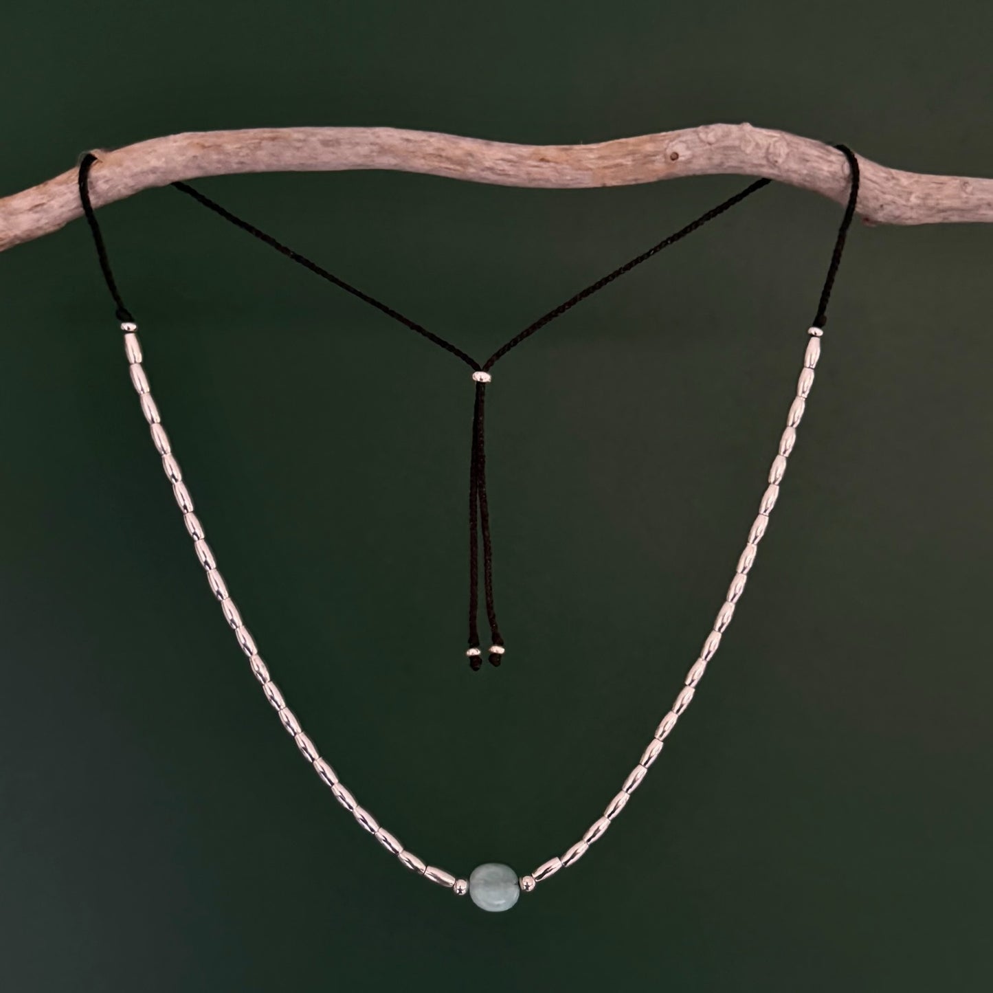 Necklace with a green bead on a branch against a dark background