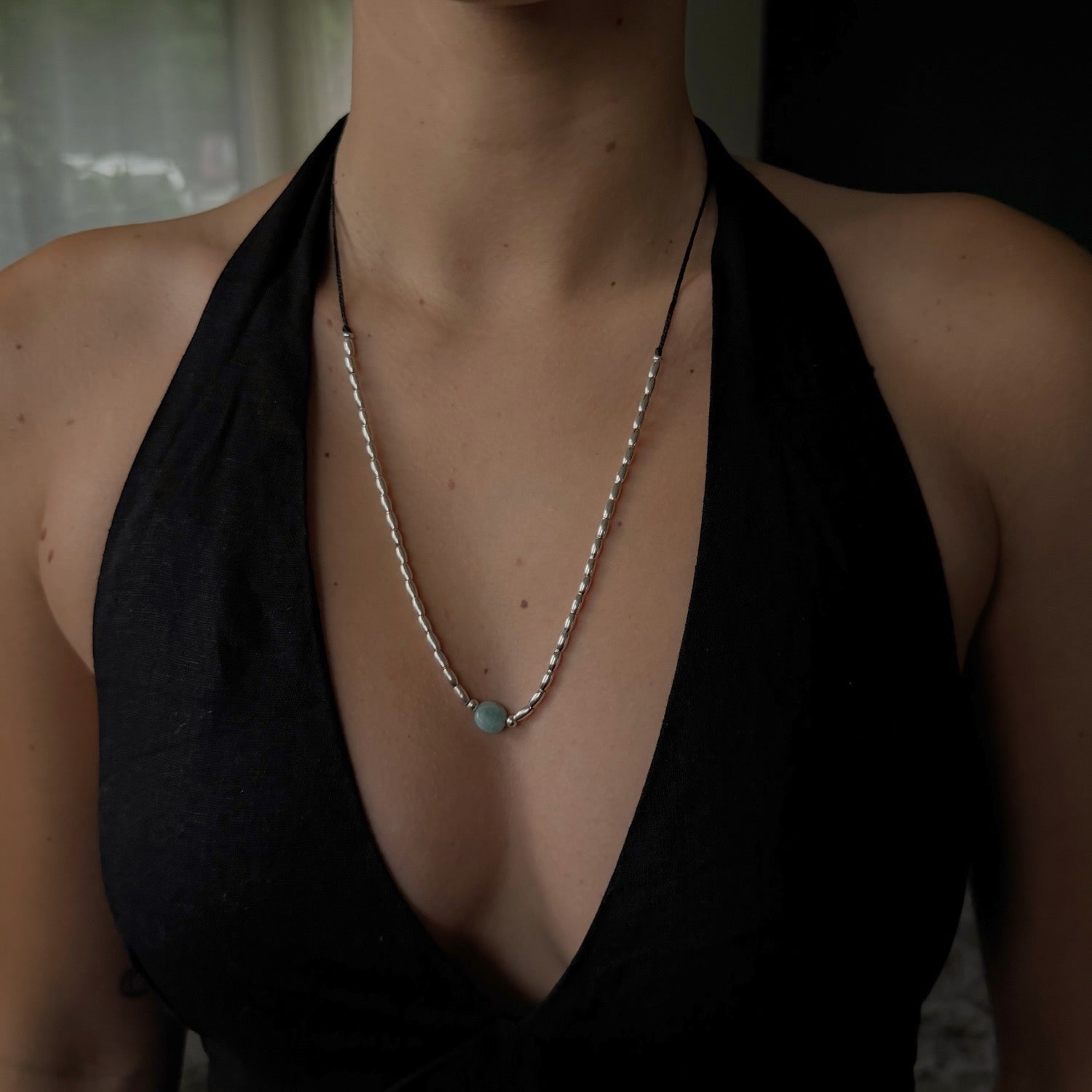 Person wearing a black halter top with a necklace featuring a green gemstone.