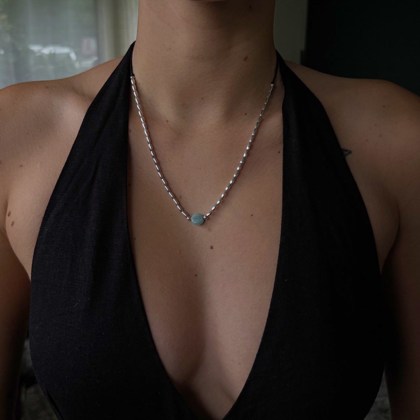 Person wearing a black top with a necklace featuring a turquoise pendant.