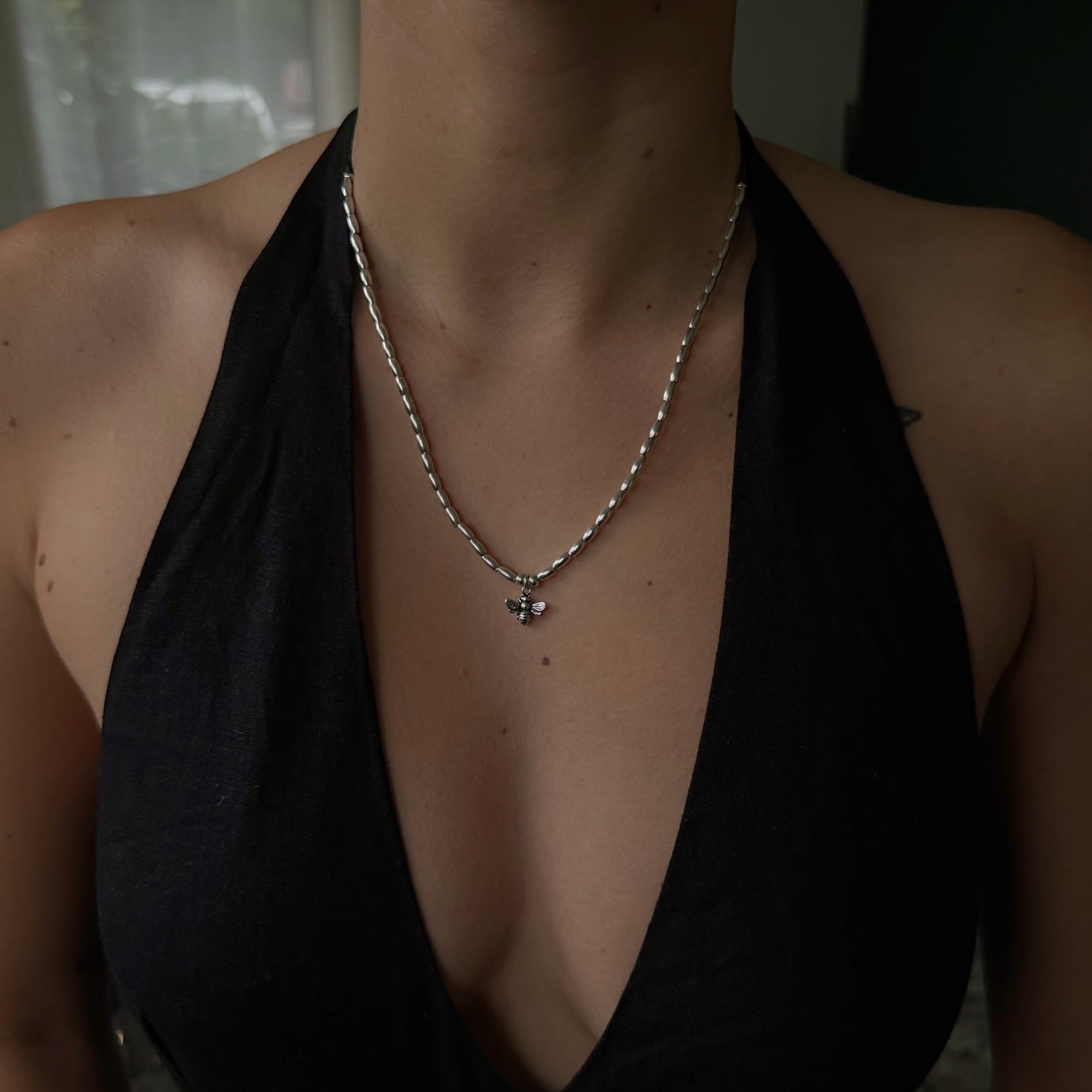 Person wearing a black halter top and silver necklace with a pendant.