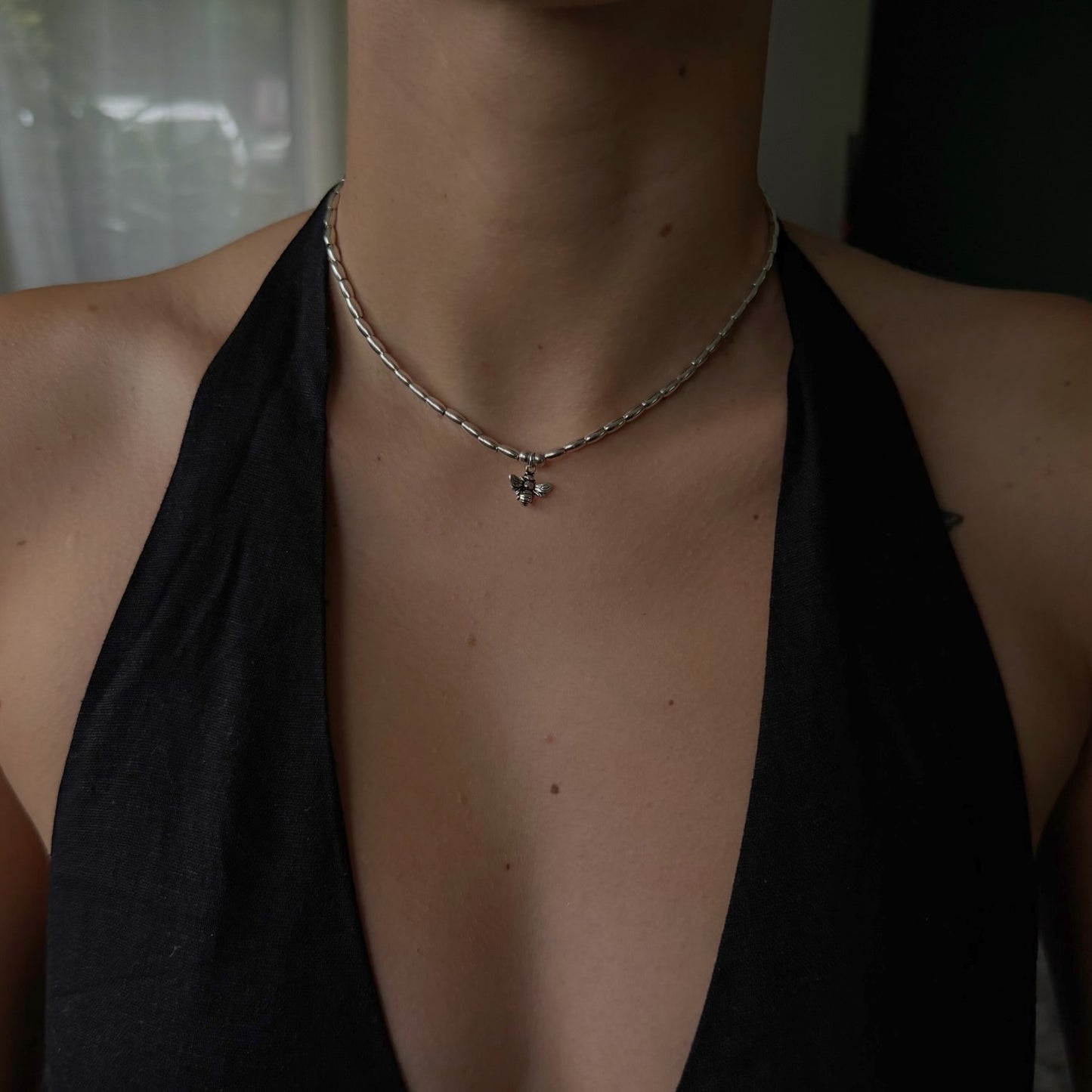 Person wearing a black top and silver necklace with a pendant.