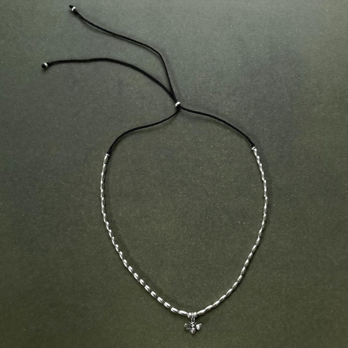 Silver beaded necklace with a small pendant on a dark green background