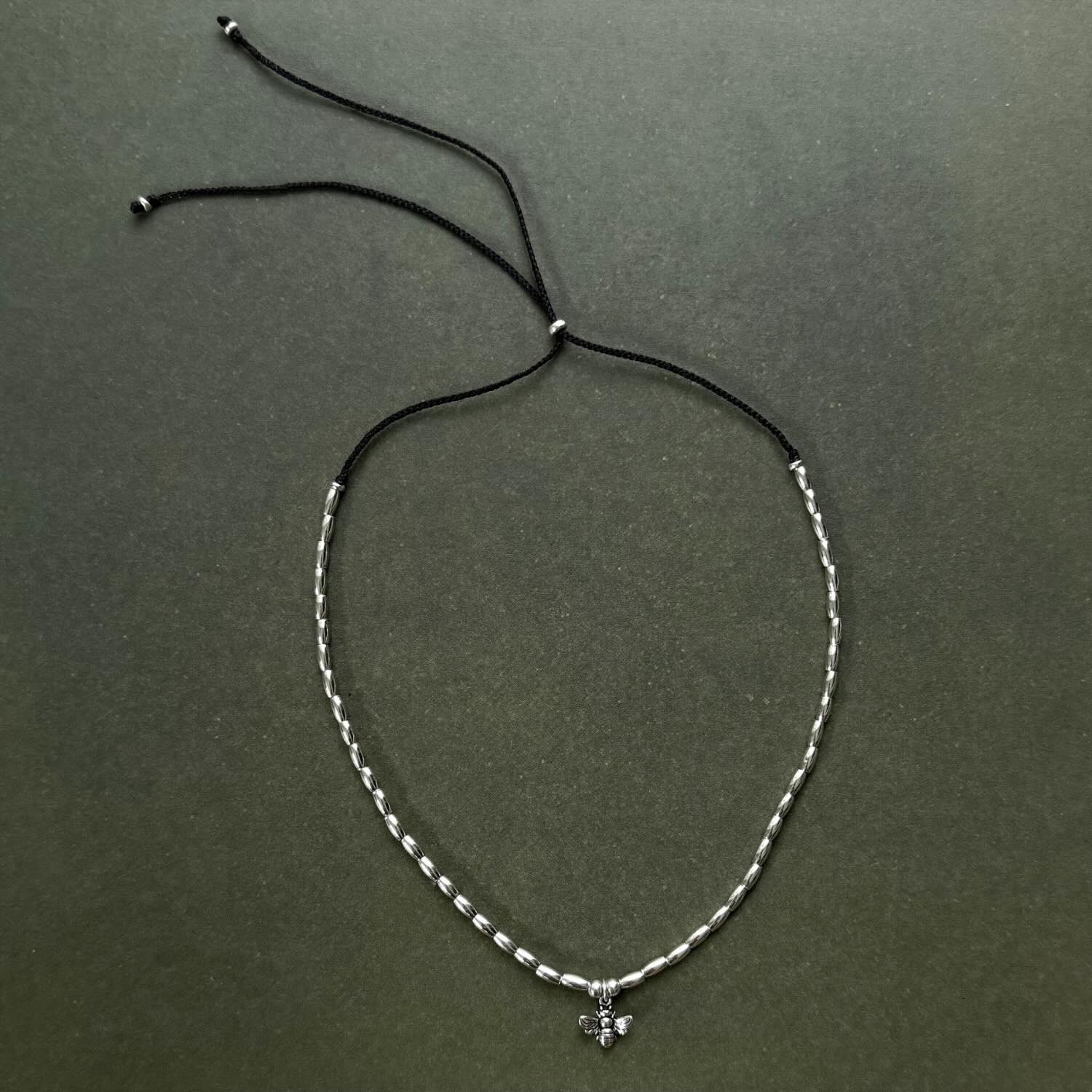 Silver beaded necklace with a small pendant on a dark green background