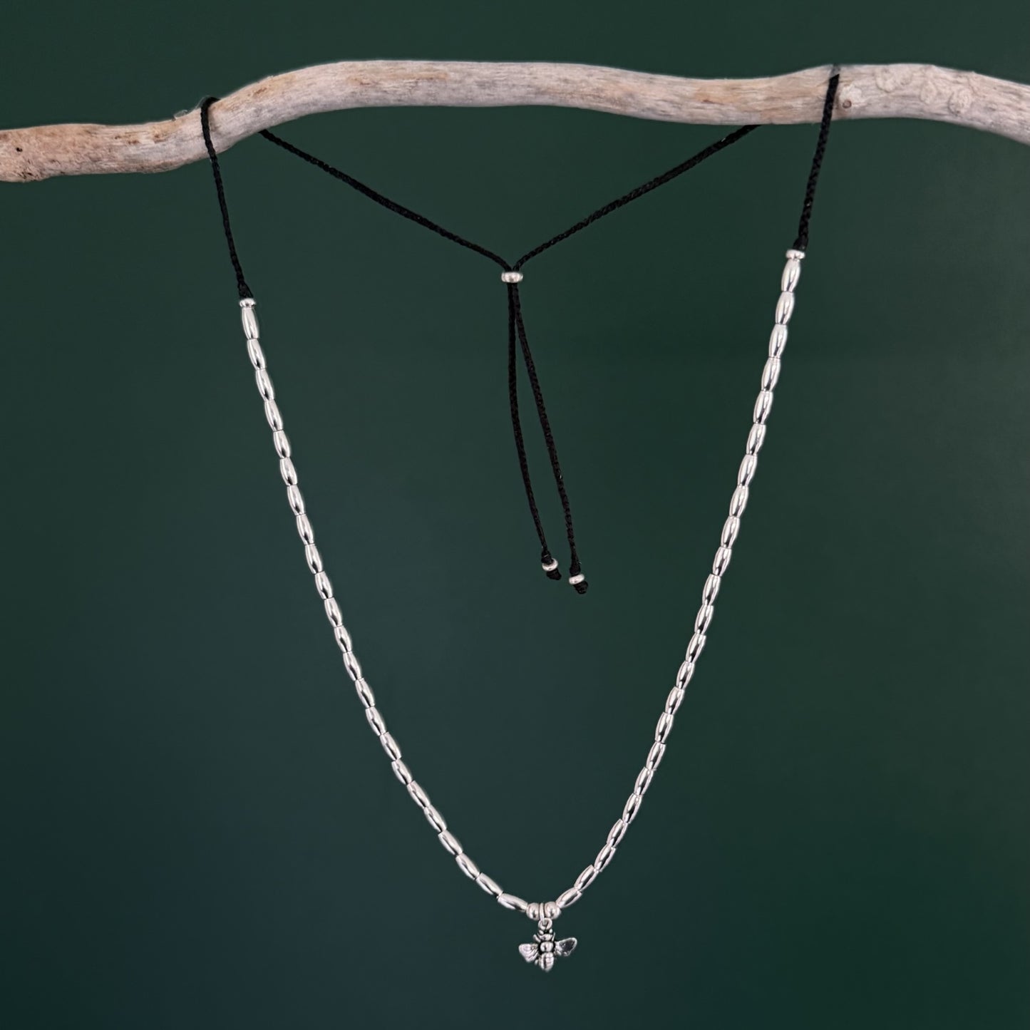 Silver chain necklace with a small pendant on a branch against a dark green background