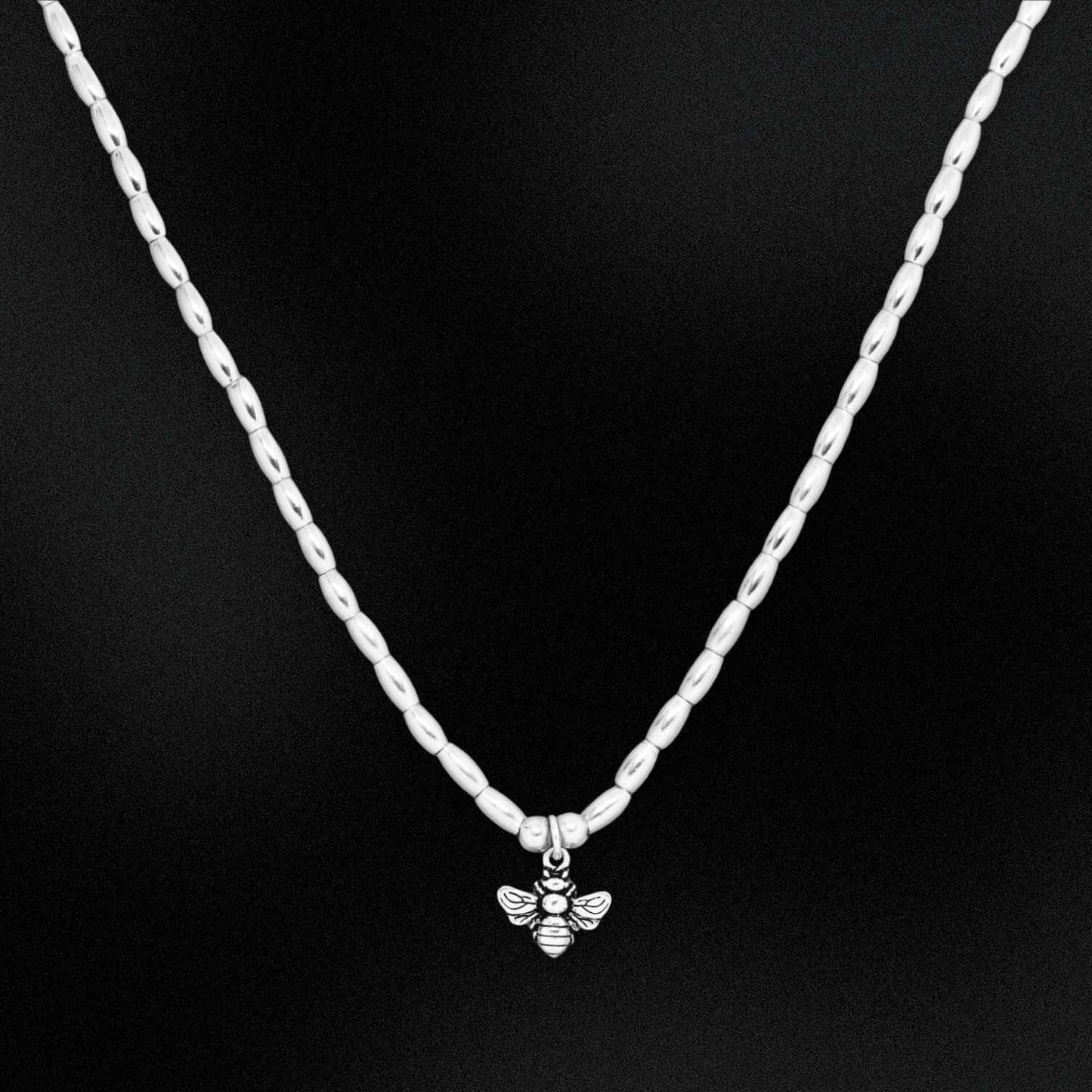 Silver chain necklace with a bee pendant on a black background