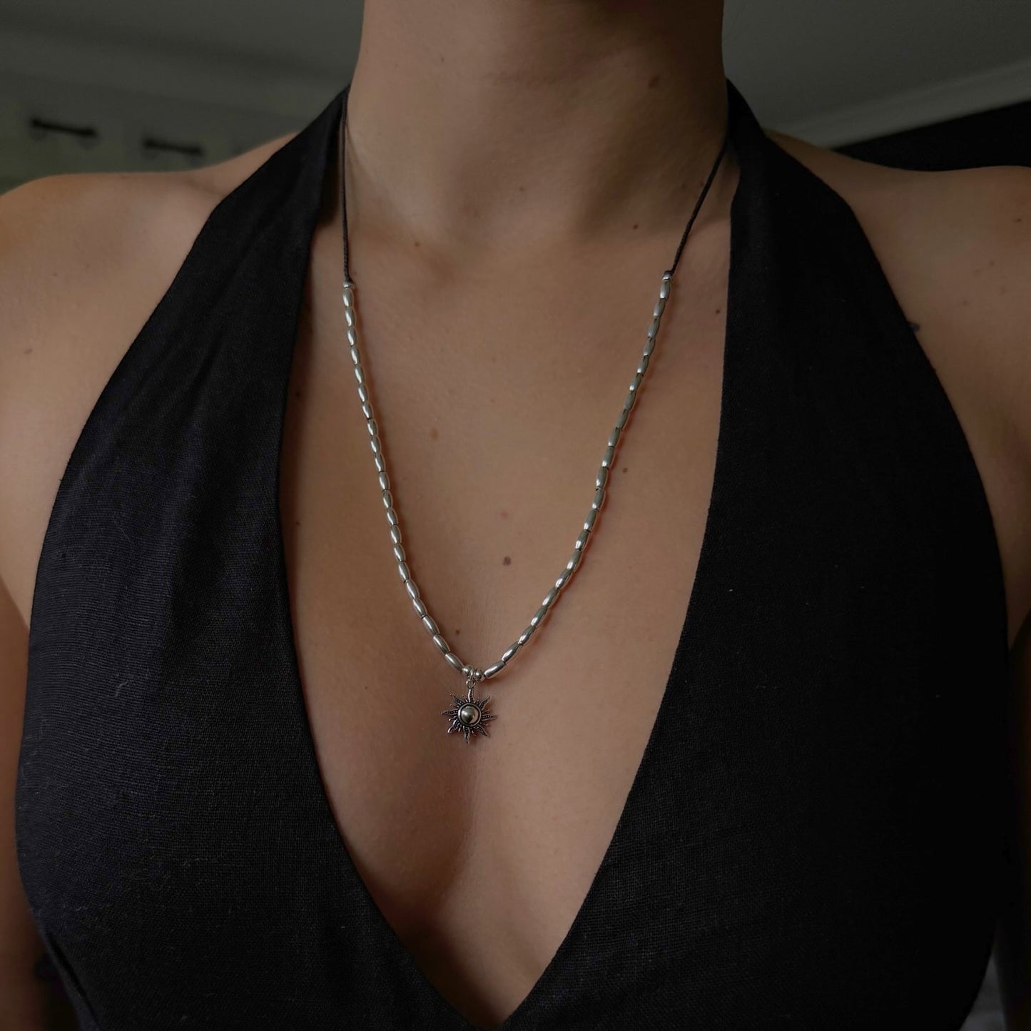 Person wearing a black top and silver necklace with a pendant.