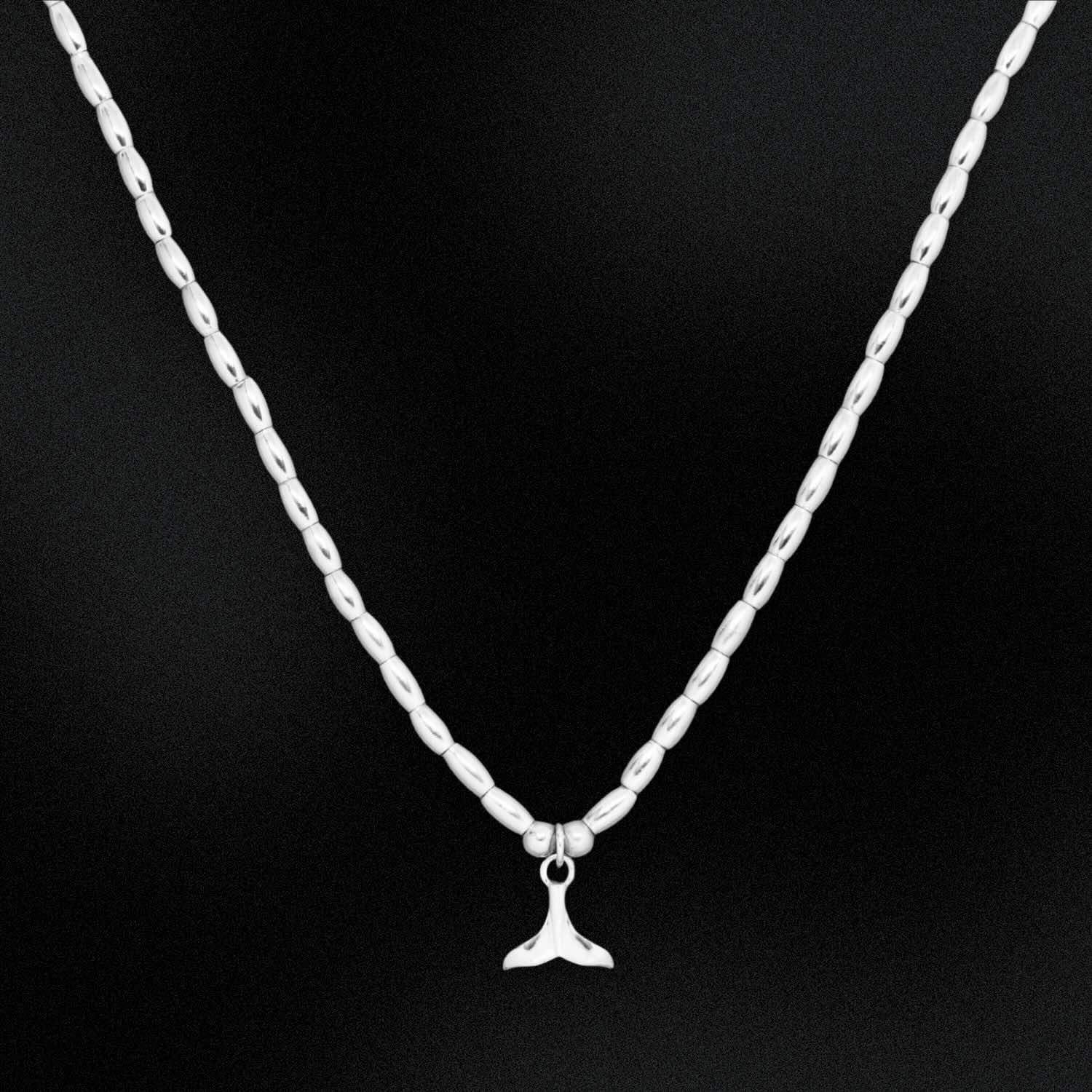 Silver chain necklace with a whale tail pendant on a black background