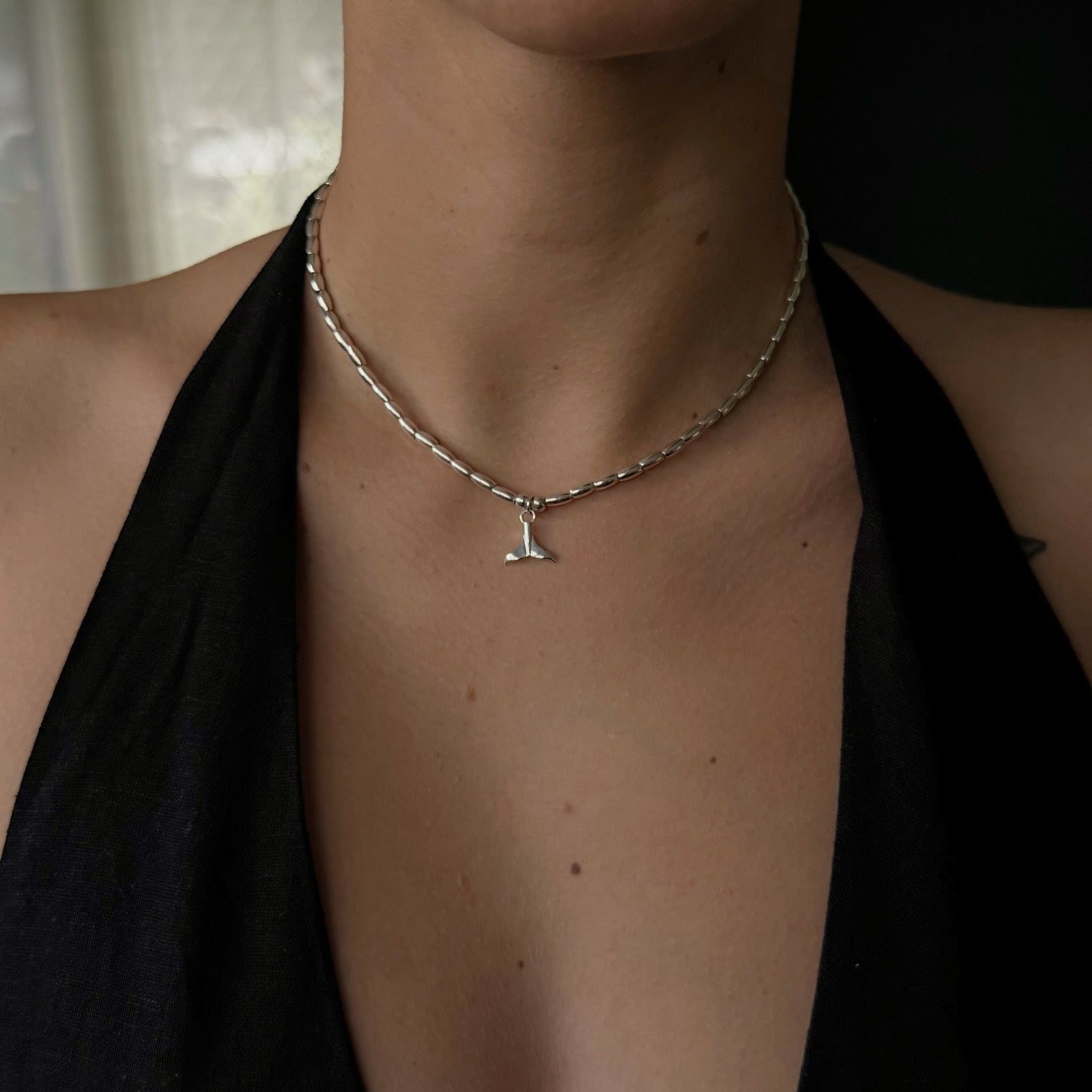 Person wearing a silver necklace with a letter 'L' pendant against a dark background