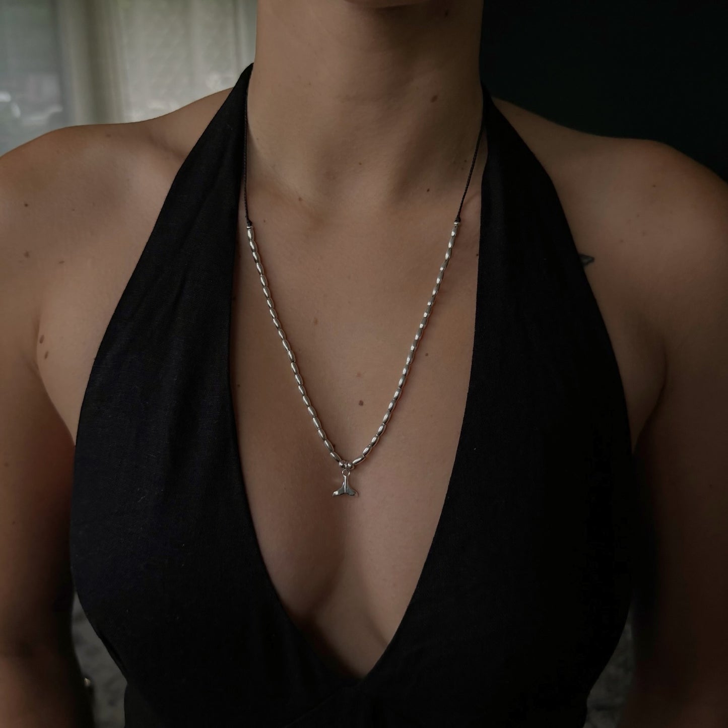 Person wearing a black halter top with a pearl necklace and pendant.
