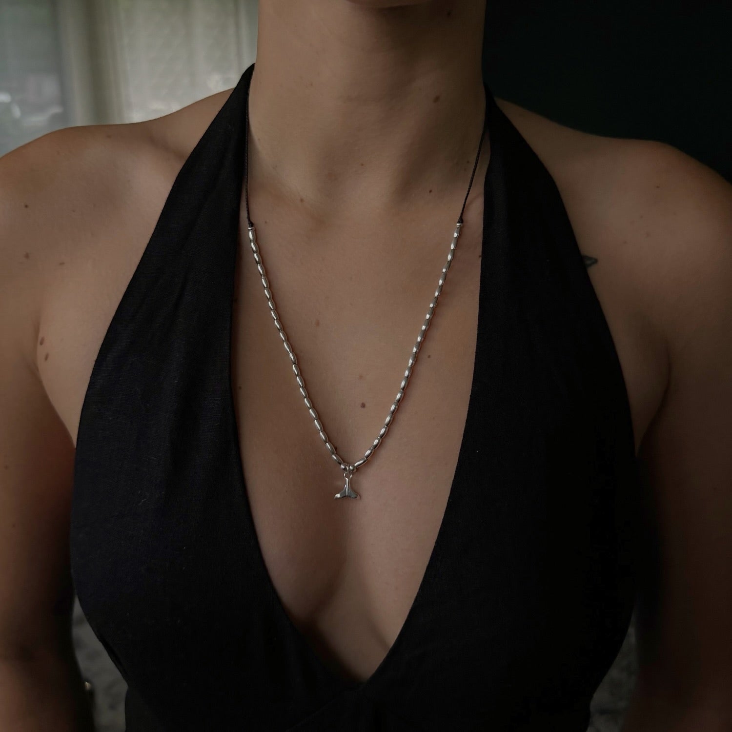 Person wearing a black halter top with a pearl necklace and pendant.
