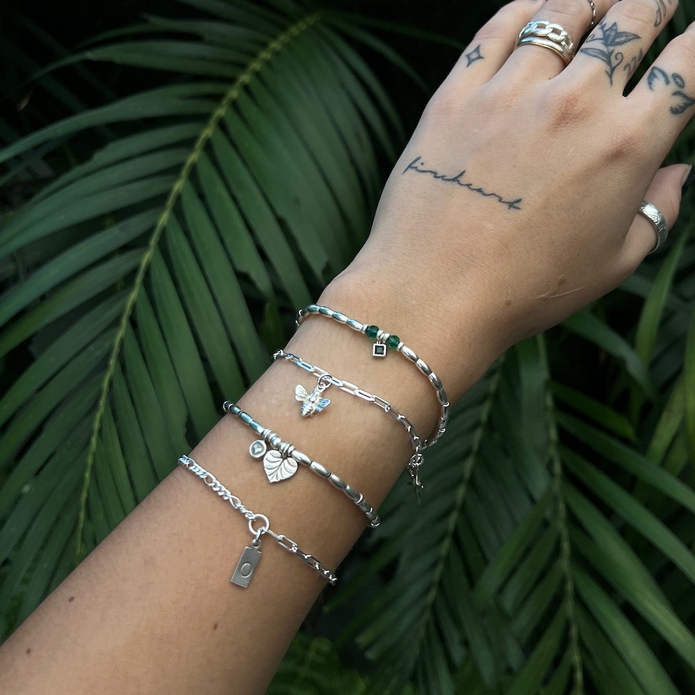 Hand wearing multiple silver bracelets with green gemstones against a green leafy background