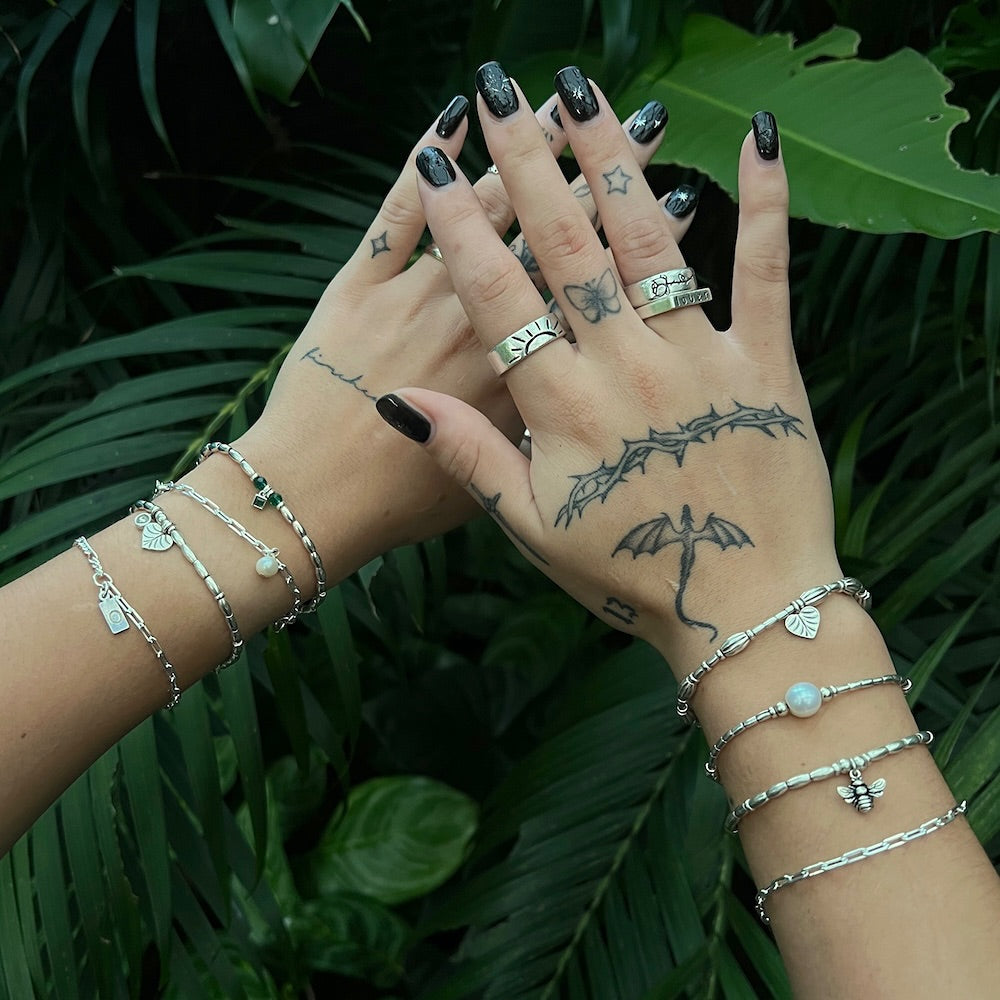 Hands with silver jewelry and tattoos against a green leafy background