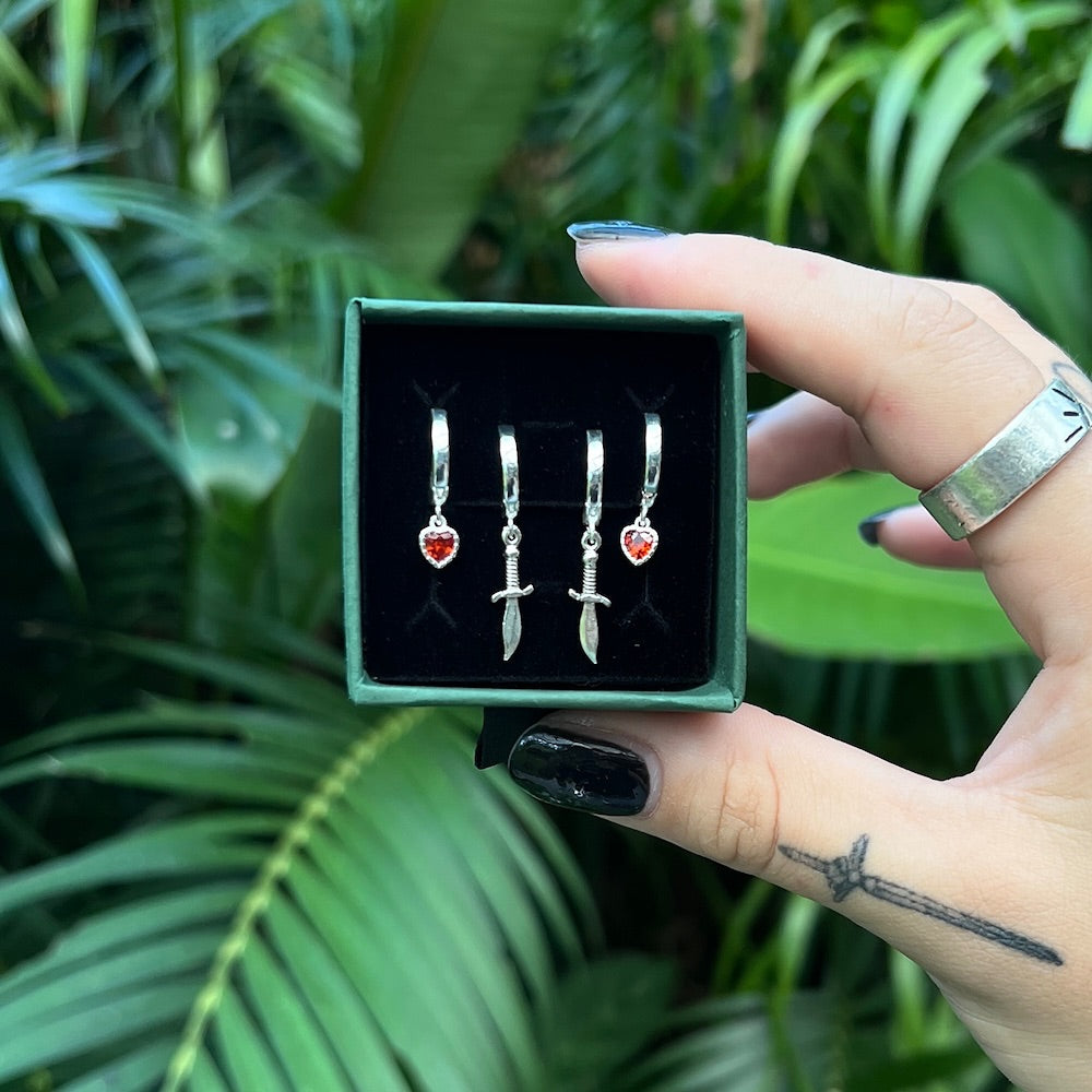 Hand holding a box of silver earrings with greenery in the background