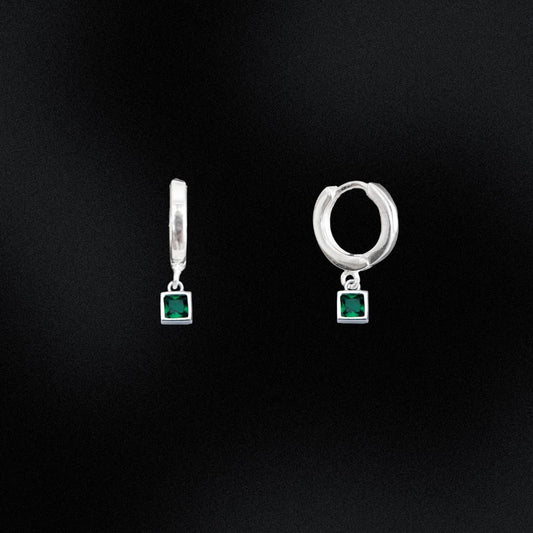 Pair of silver hoop earrings with green gemstones on a black background