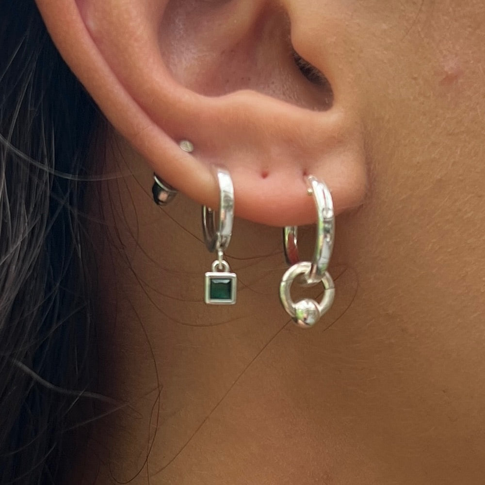 Close-up of an ear wearing silver hoop earrings with a green gemstone charm.