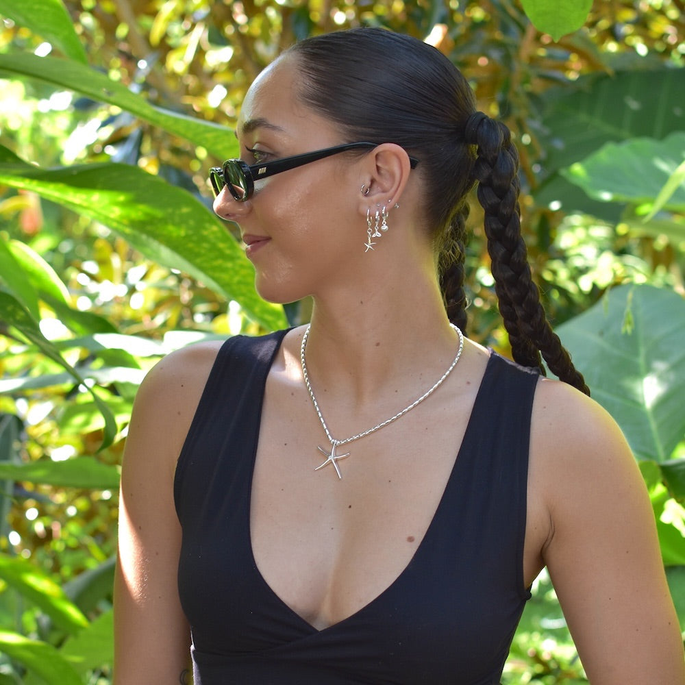 Woman wearing sunglasses and a black top with green foliage in the background