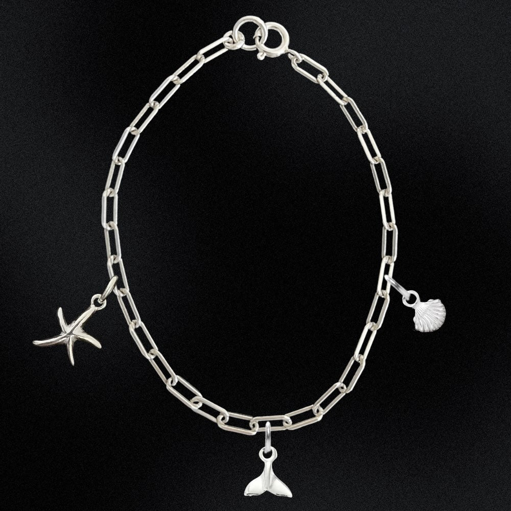 Silver chain bracelet with starfish, shell, and whale tail charms on a black background