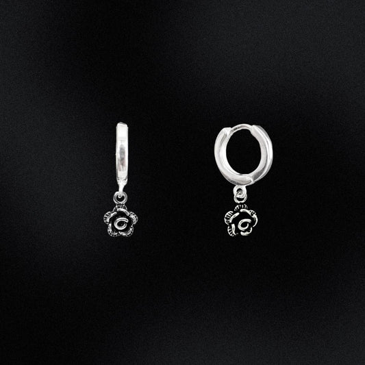 Pair of silver hoop earrings with rose-shaped charms on a black background