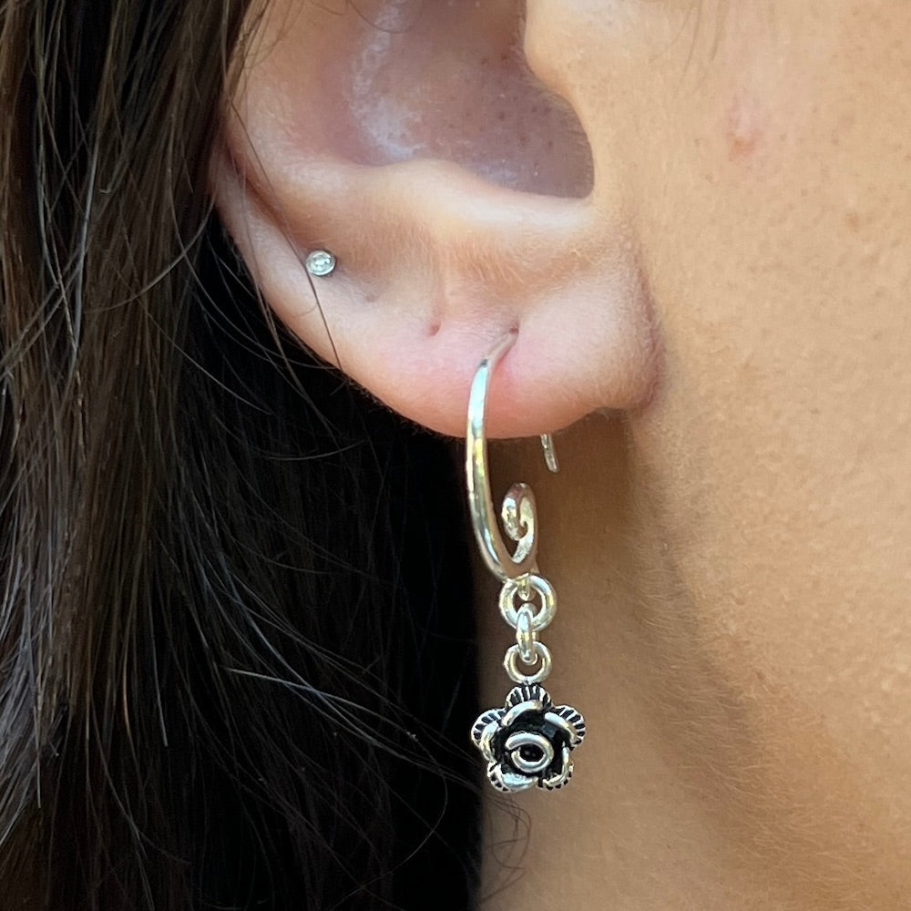 Close-up of an ear wearing a silver hoop earring with a floral charm.