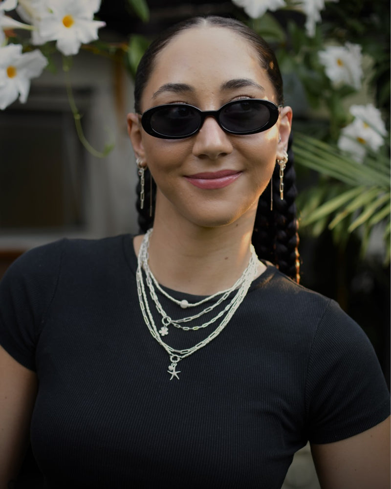 Woman wearing sunglasses and layered necklaces with a blurred floral background