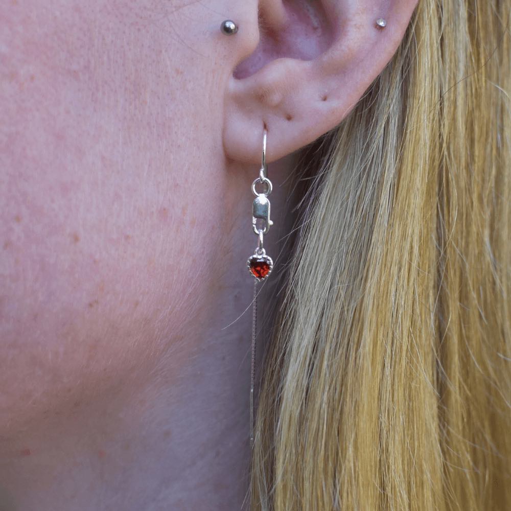 Introducing our Sterling Silver Flaming Heart Threader Earrings, the perfect way to add some passion and flare to your jewellery collection. These earrings are crafted from high-quality sterling silver and are adorned with tiny red heart charms that symbolise love and courage.  Our threader earrings are incredibly versatile and easy to wear, making them perfect for any occasion. The flaming hearts add a touch of warmth and energy, making them perfect for any free-spirited, passionate individual.