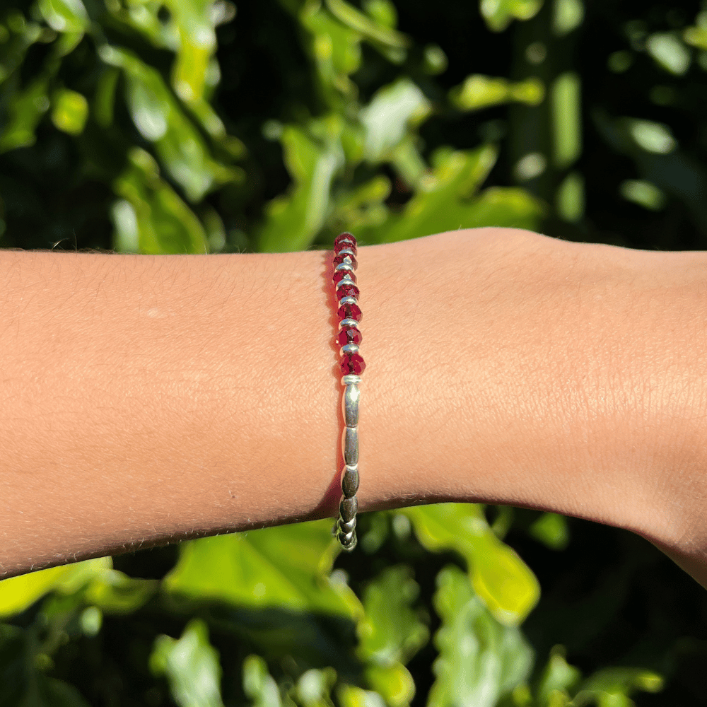 Introducing the Ruby Essence Silver Beaded Bracelet - the perfect accessory to complete any outfit. The centre detail of the bracelet features stunning faceted glass rondelle red beads that catch the light and sparkle brilliantly. Surrounding these gems are delicate silver beads, adding a touch of sophistication and elegance to the design.