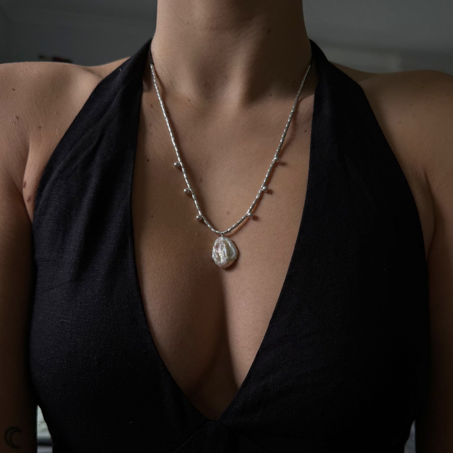 Person wearing a black top with a deep neckline and a necklace with a pendant.