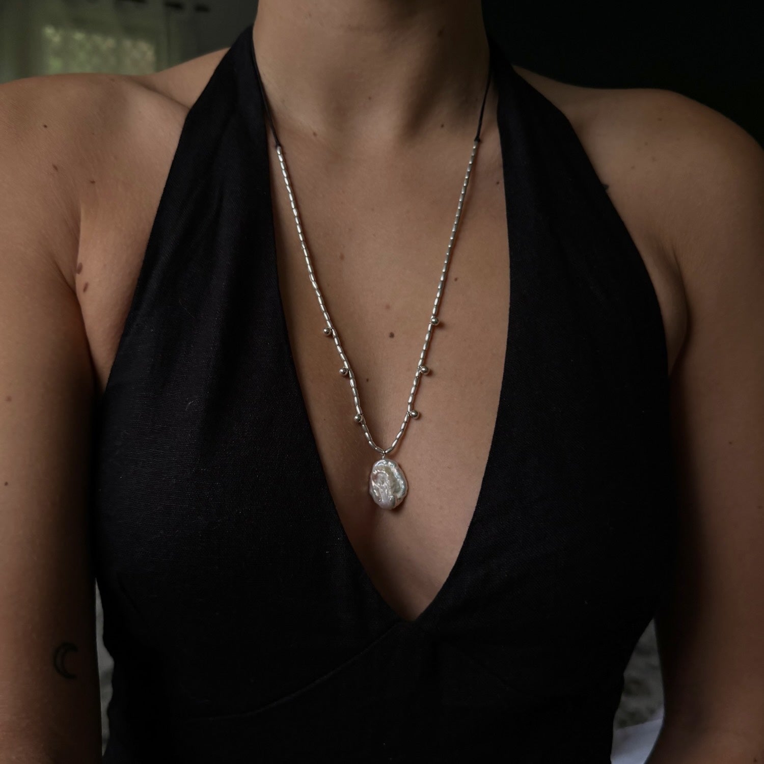 Person wearing a black top with a necklace featuring a large pendant.