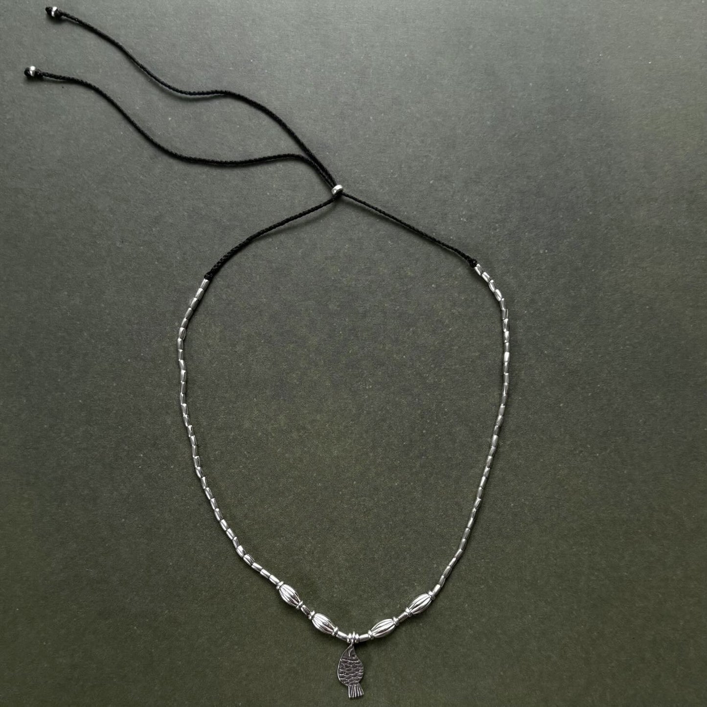 Necklace with beads and a small charm on a dark green background