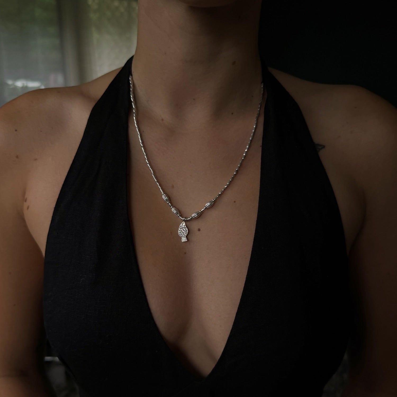 Person wearing a black halter top with a necklace featuring a pendant.